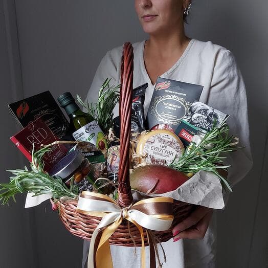 A large red-green basket with mangoes. Slicing, cheese, sausage, olives, chocolate and oil